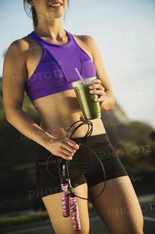 Young woman holding jump rope and smoothie