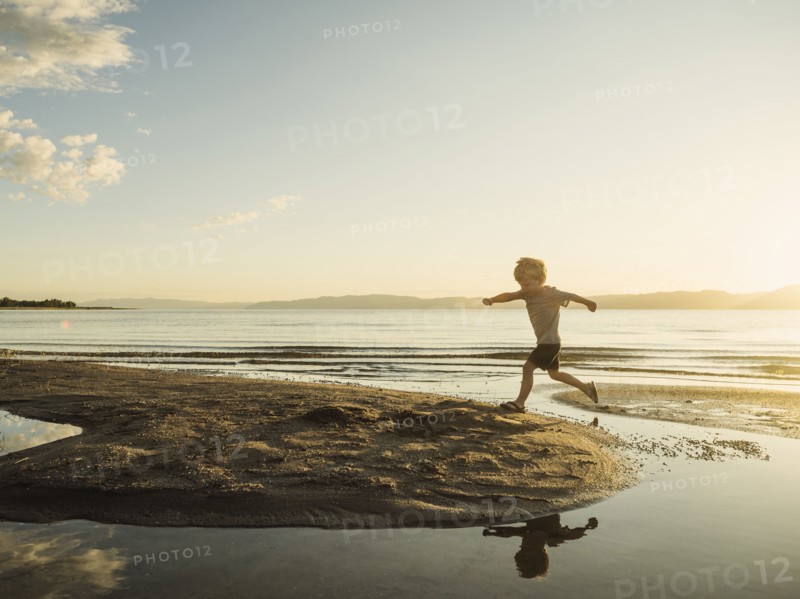 Small boy (4-5) jumping over water on sunny day