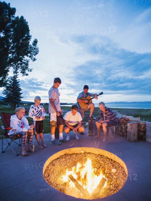 Parents with children (8-9, 10-11, 16-17) sitting in front of campfire and playing guitar