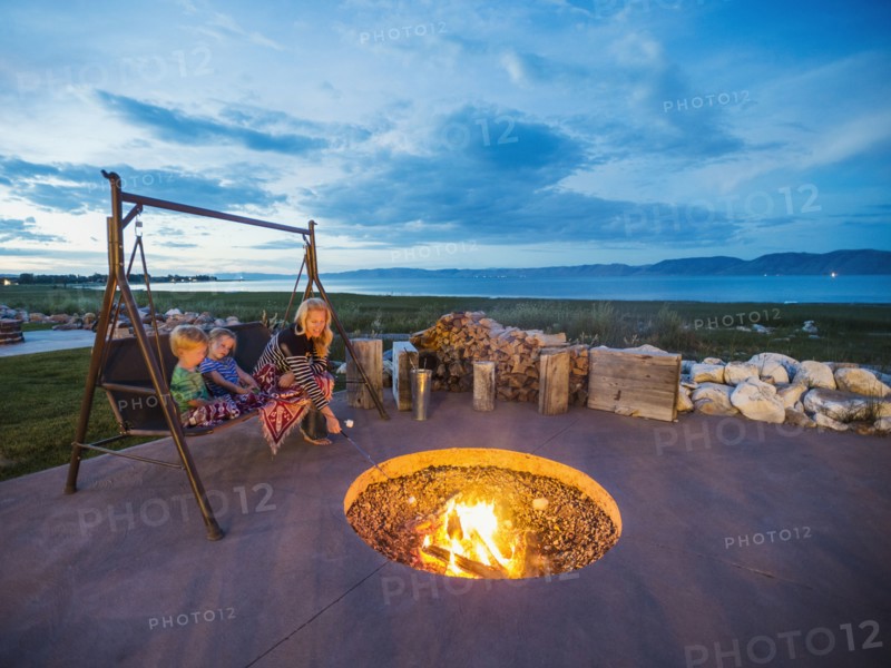 Mother with children (4-5) sitting on wooden swing in front of campfire