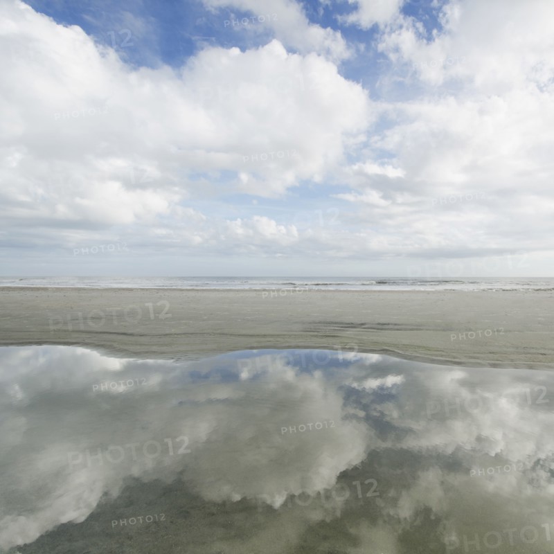 Reflection of clouds in puddle, sea in background