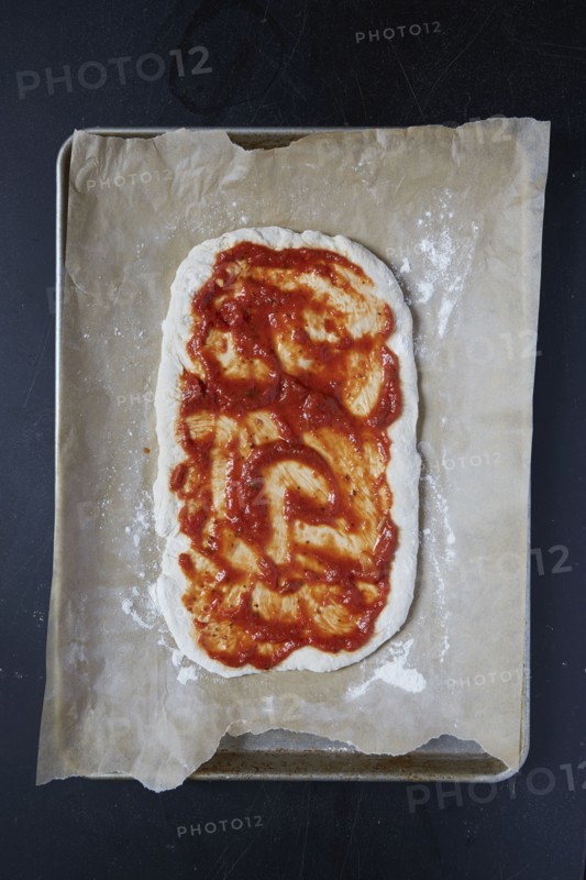 Pizza dough with tomato sauce on wax paper