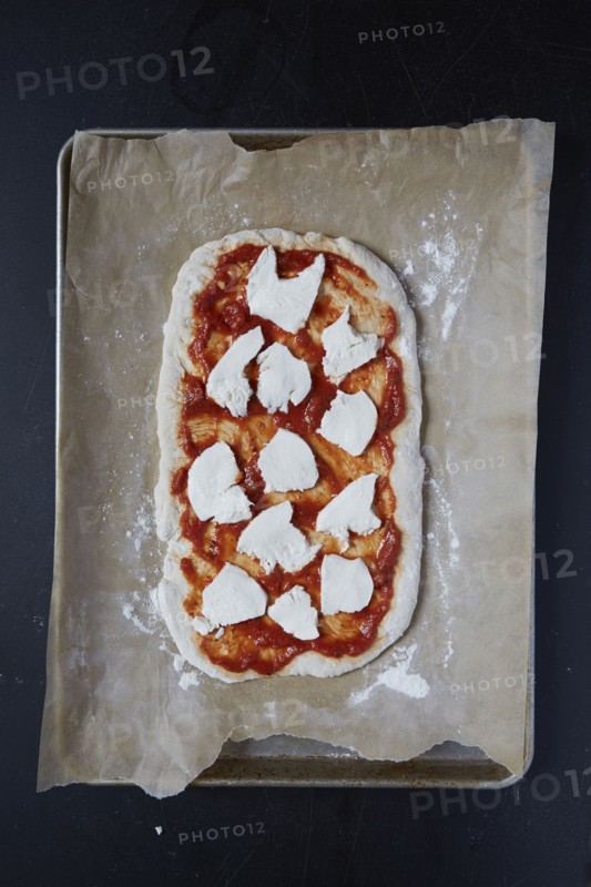 Pizza dough with tomato sauce and mozzarella on wax paper