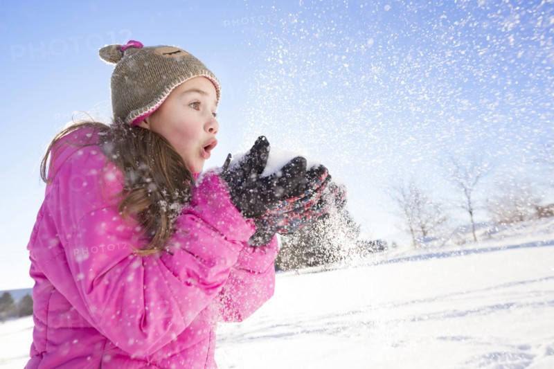 Girl (10-11) in pink jacket blowing snow