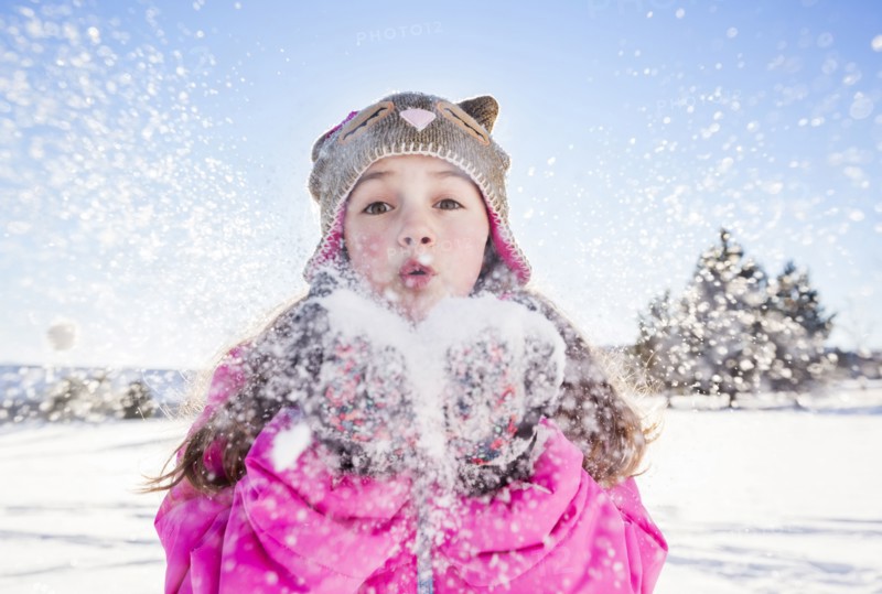 Girl (10-11) in pink jacket blowing snow