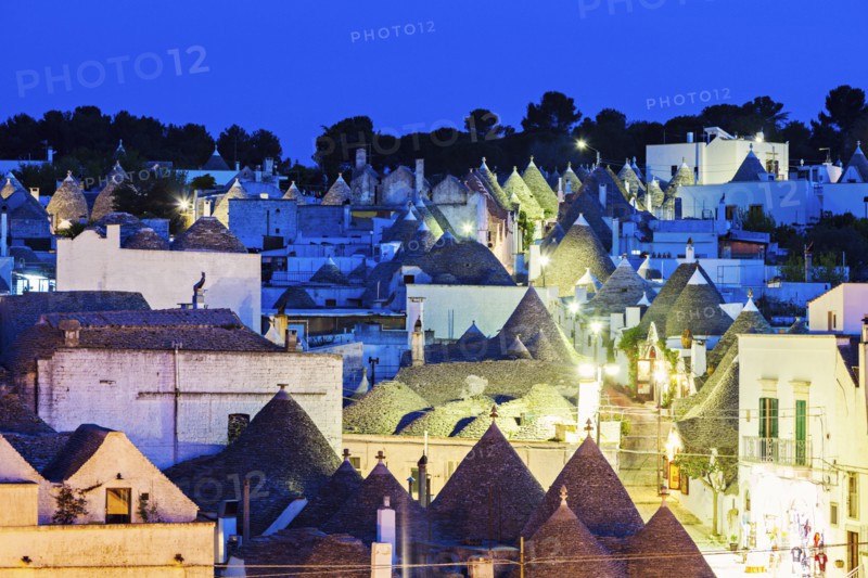 Trulli houses along illuminated street under blue sky
