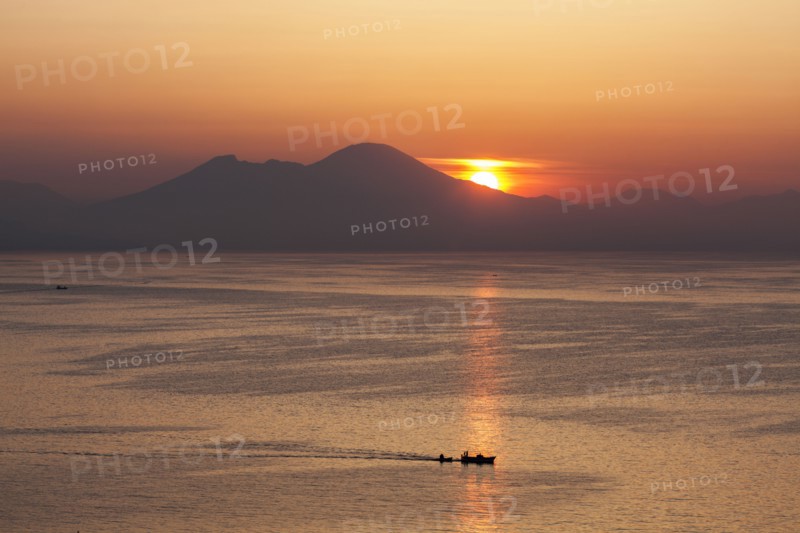 Silhouette of boat on sea with mountains in background at sunset