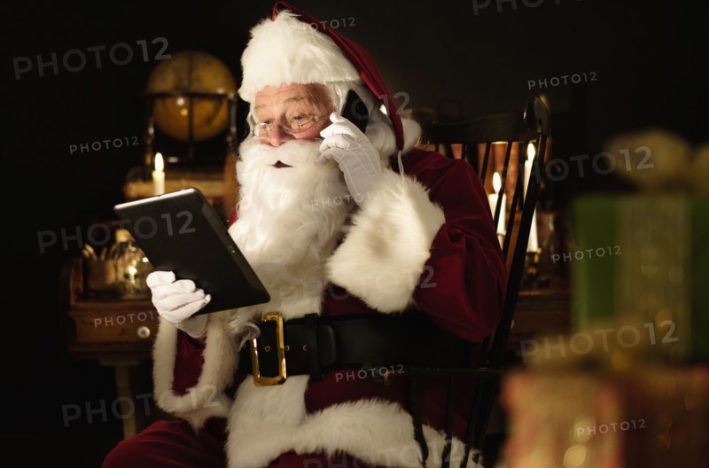 Santa Claus using digital tablet and talking by mobile phone.