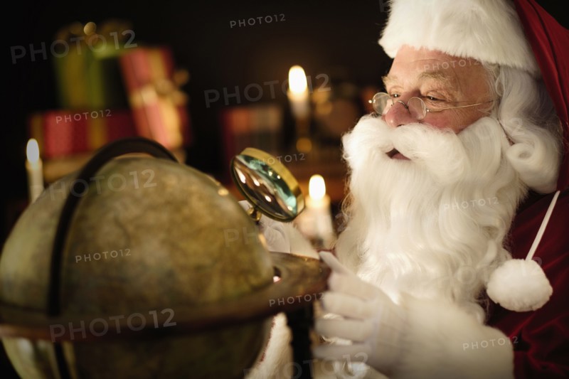 Santa Claus looking through magnifying glass at globe.