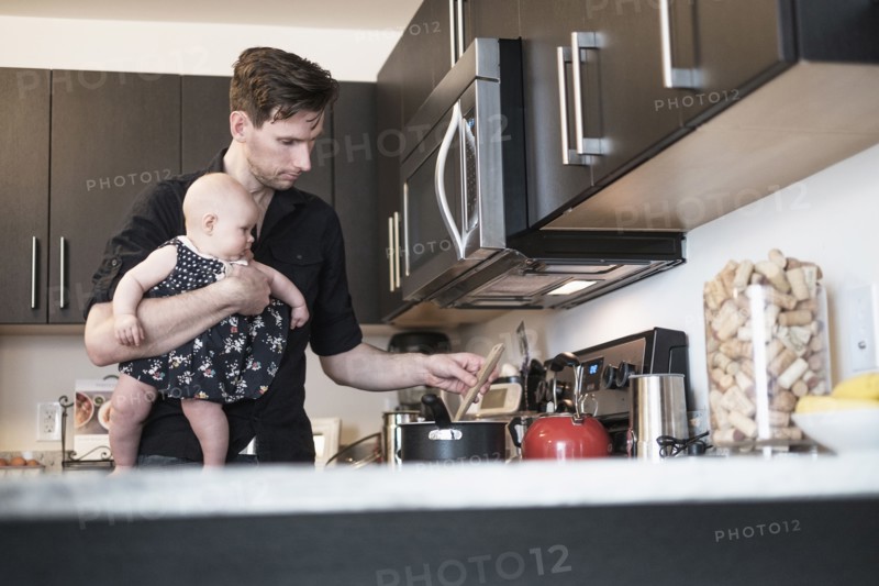 Father holding baby daughter (2-5 months) while stirring food.