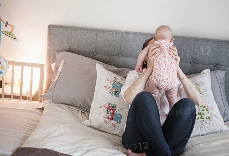 Mother playing with baby daughter (2-5 months) in bedroom.