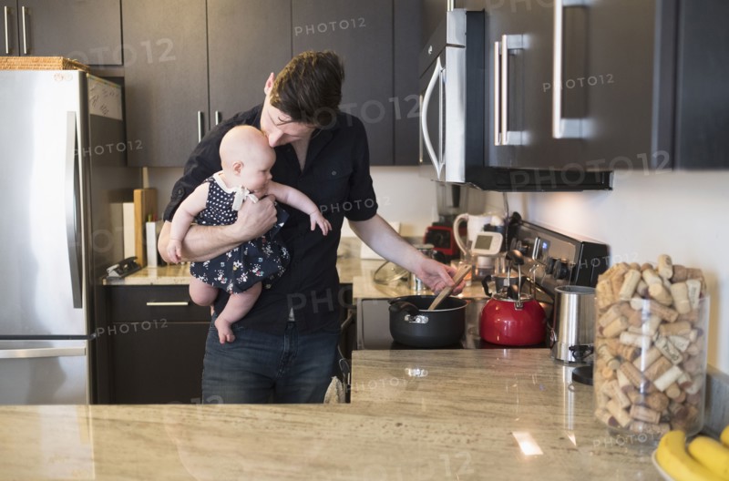 Father kissing baby daughter (2-5 months) while stirring food.