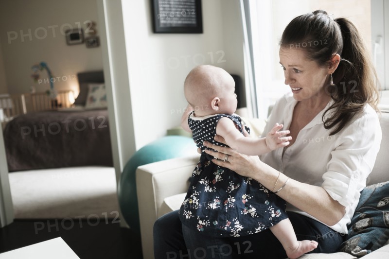 Mother playing with baby daughter (2-5 months) in living room.