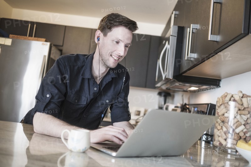 Man smiling while working on laptop computer in kitchen.