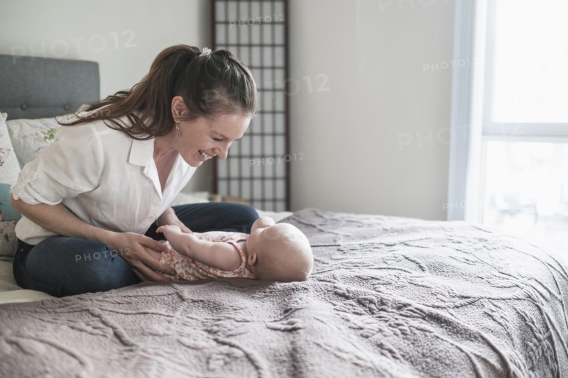 Mother playing with baby daughter (2-5 months) in bedroom.