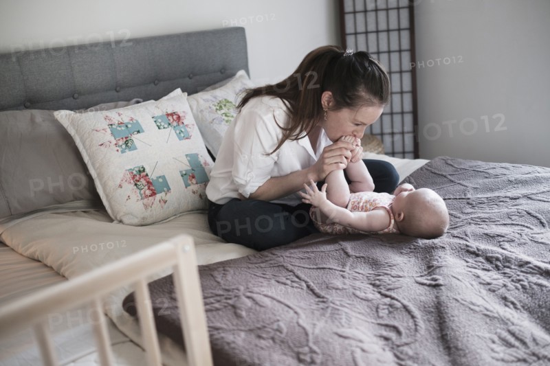 Mother kissing baby daughter's (2-5 month) feet in bedroom.