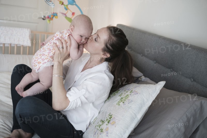 Mother kissing baby daughter (2-5 months) in bedroom.