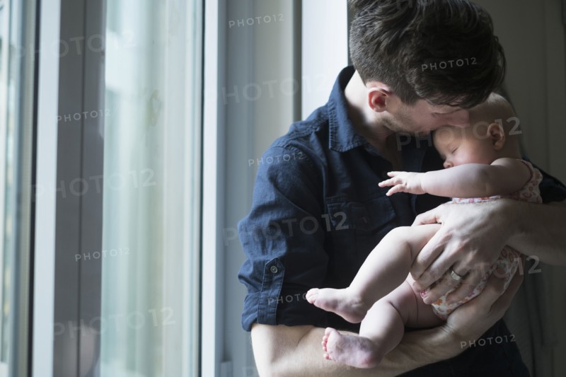 Father standing by window with daughter (2-5 months).