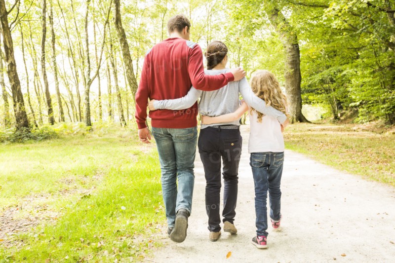 Daughter (8-9) with parents walking in park, rear view