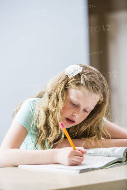 Blonde girl (8-9) doing homework at table