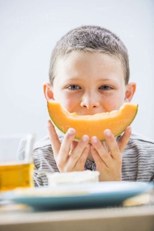 Little boy (6-7) eating cantaloupe for breakfast