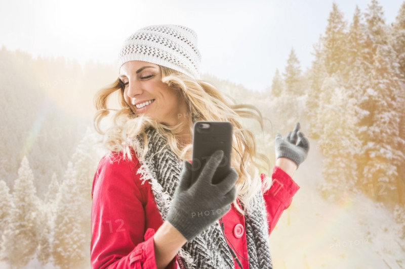 Young woman wearing winter clothing dancing with smart phone in hands