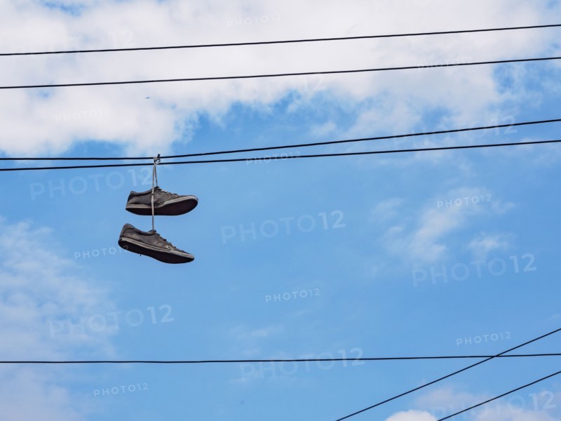 Pair of shoes hanging on cable lines against sky