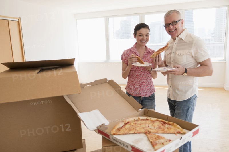 Portrait of smiling couple eating pizza in new apartment.