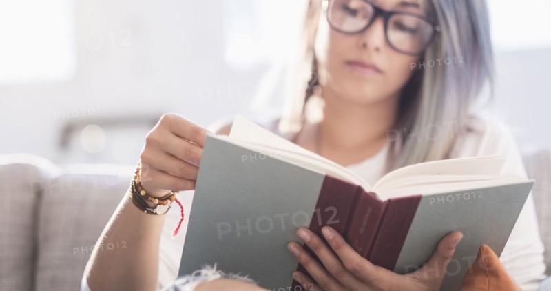 Young woman sitting on sofa and reading book.
