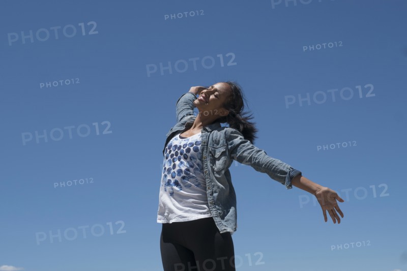 Mid adult woman outstretching her arms against blue sky.