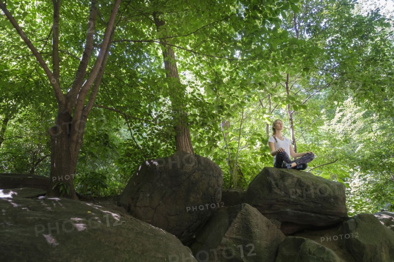 Young woman meditating on rocks in woodland.