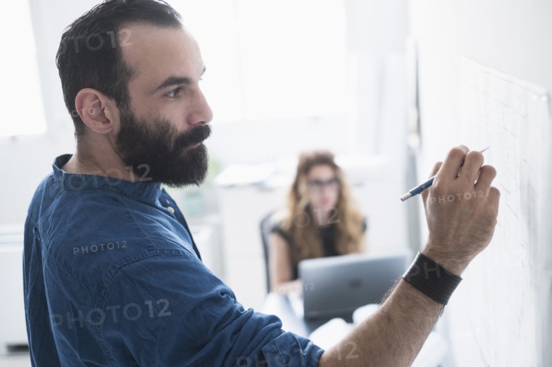Mid-adult man writing on whiteboard.