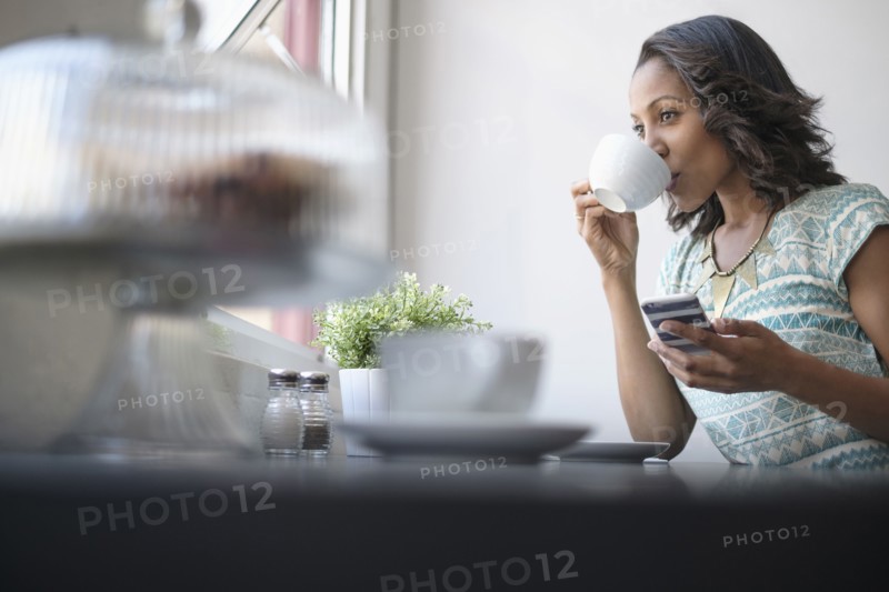 Woman drinking coffee and using phone.