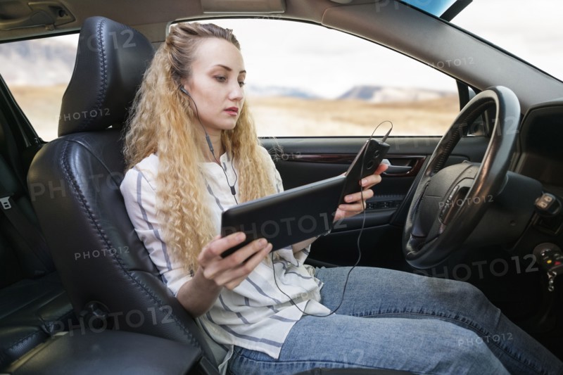 Woman sitting in car and using tablet and mobile phone at same time.