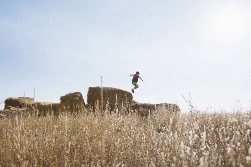 Boy (6-7) jumping on bale of hay