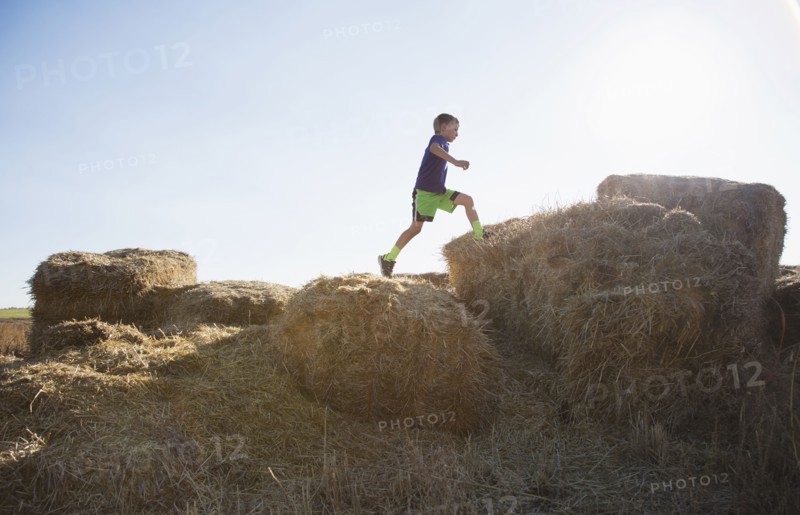 Boy (6-7) running on straw bales at sunset