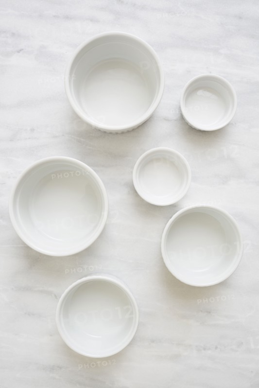 Overhead view of empty white ceramic bowls on marble table