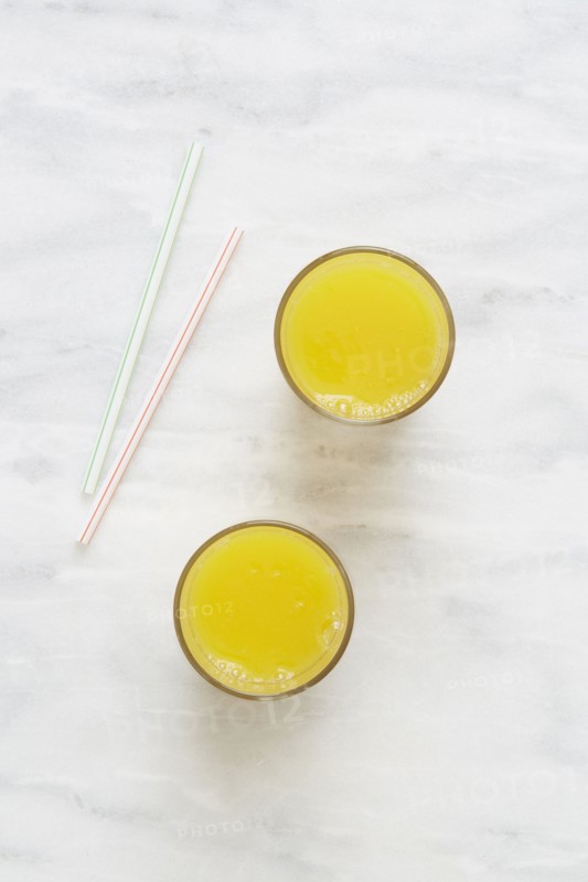 Overhead view of glass of orange juice and drinking straws