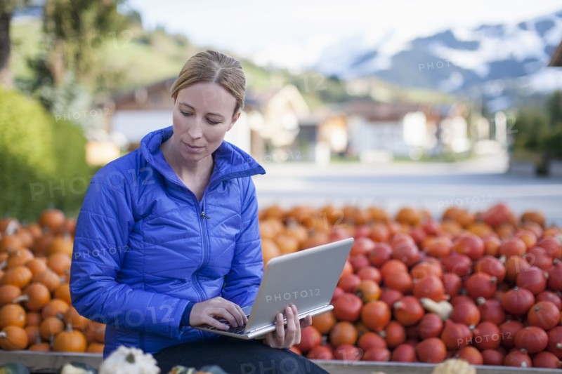 Austria, Salzburger Land, Maria Alm, Mature woman in blue jacket using laptop in market stall
