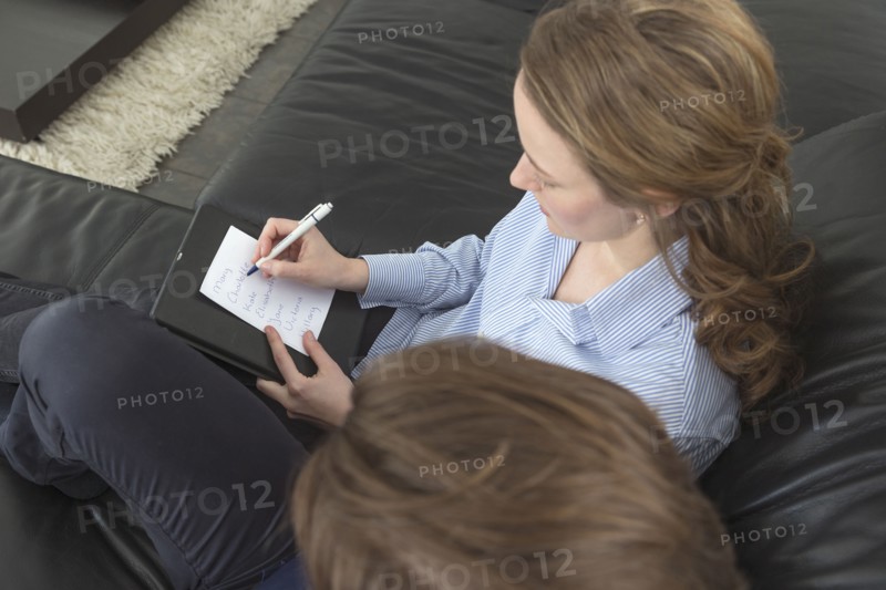 Woman sitting on sofa next to man and writing