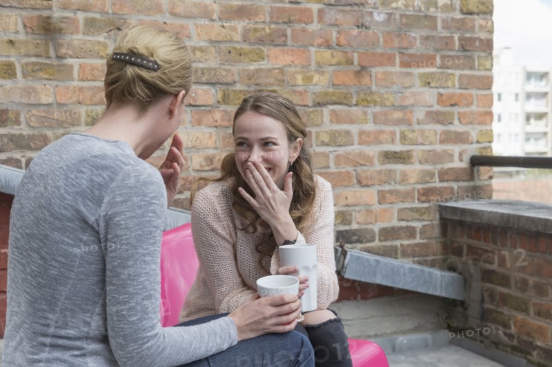 Women gossiping while sitting on balcony with coffee cups