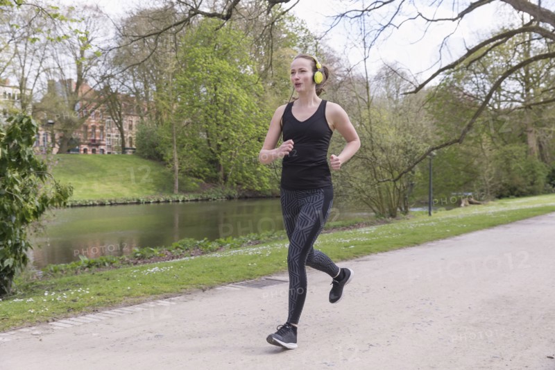Mid-adult woman with headphones on jogging by canal in park