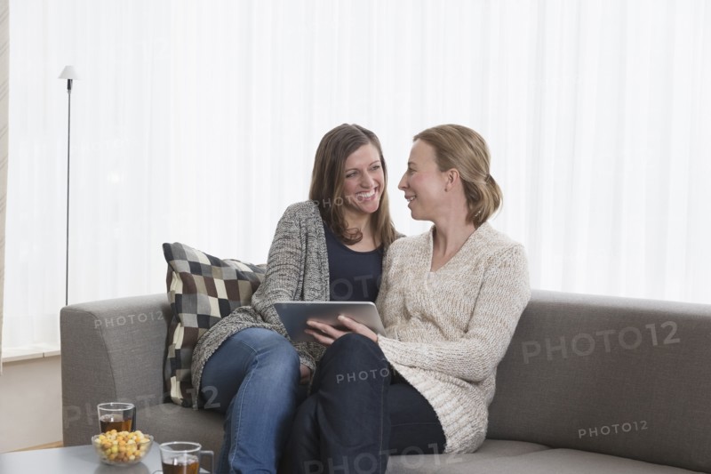 Smiling women sitting on sofa in living room and holding tablet