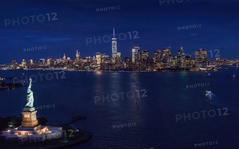 USA, New York, New York City, Manhattan, Aerial view of illuminated skyline with Statue of Liberty at night.