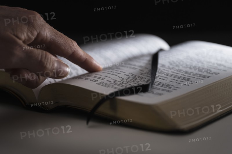 Human finger on open Bible.