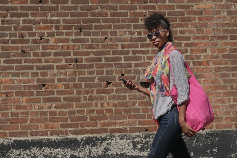 Young woman walking against brick wall.