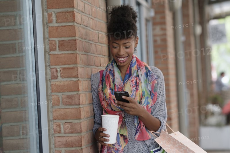 Young woman with shopping bags leaning against brick wall.