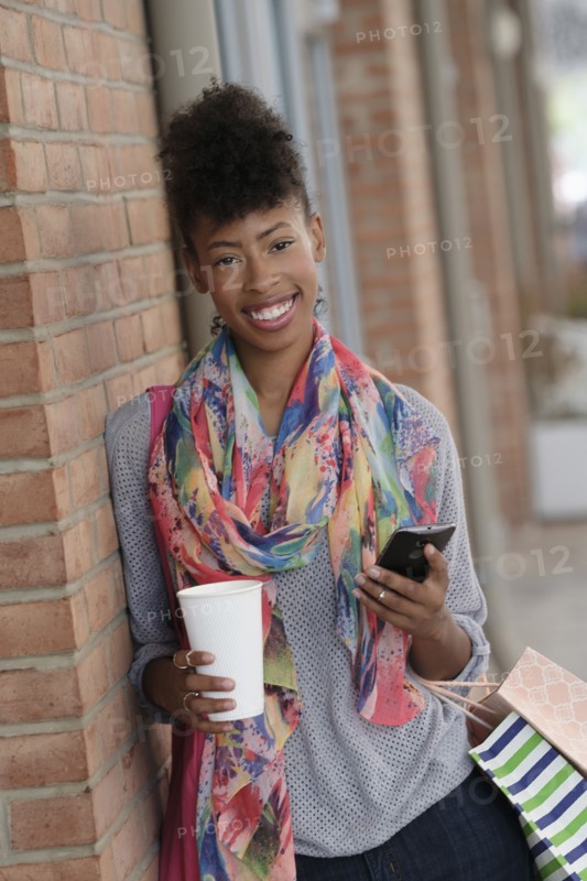 Young woman with shopping bags leaning against brick wall.