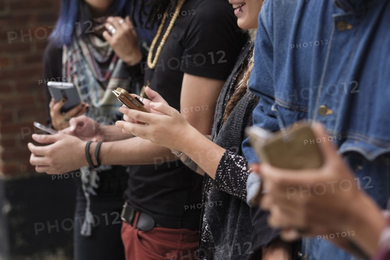 Young people standing in row using smartphones.