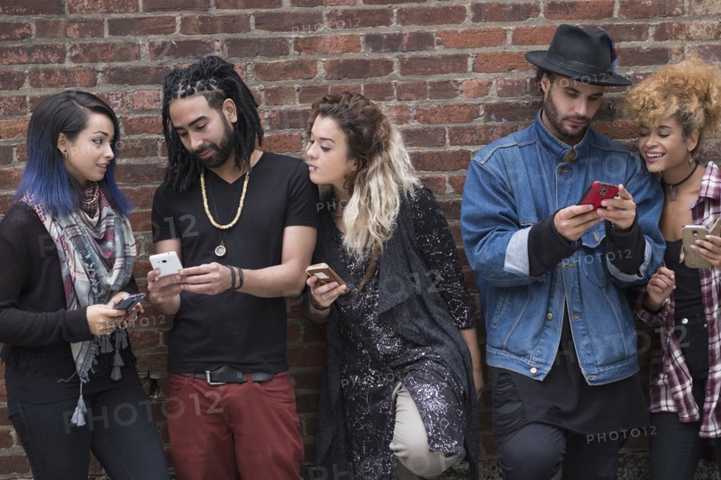 Portrait of friends using smartphones against brick wall.